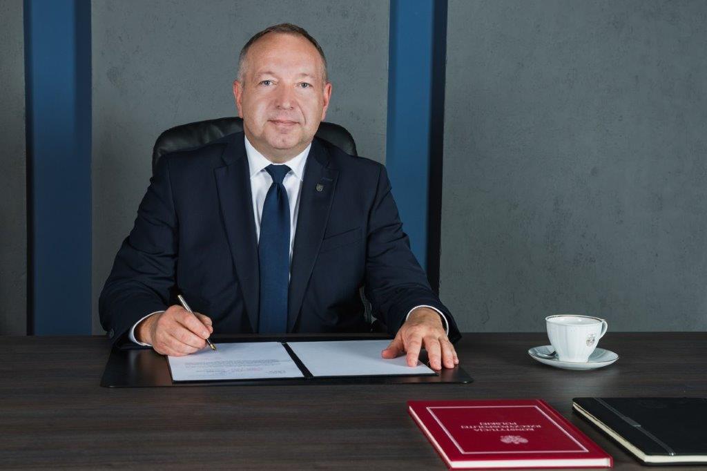 Prezydent Miasta podpisuje dokumenty, po prawej stoi filiżanka z herbem miasta, z przodu w czerwonej okładce Konstytucja RP
